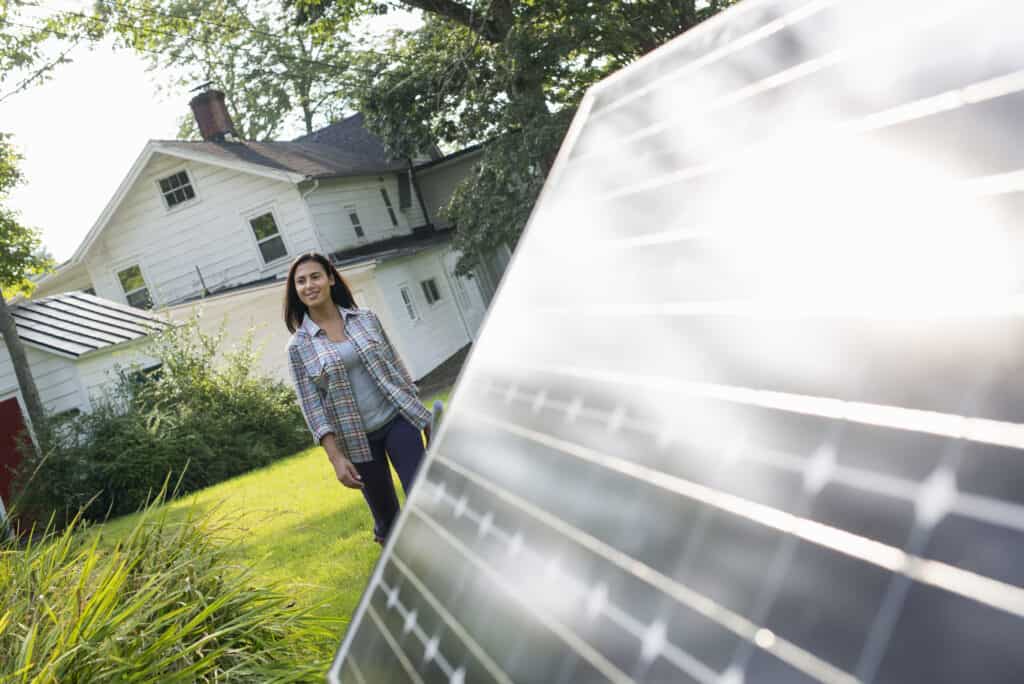 woman in front of a house, in the yard, next to a solar panel
